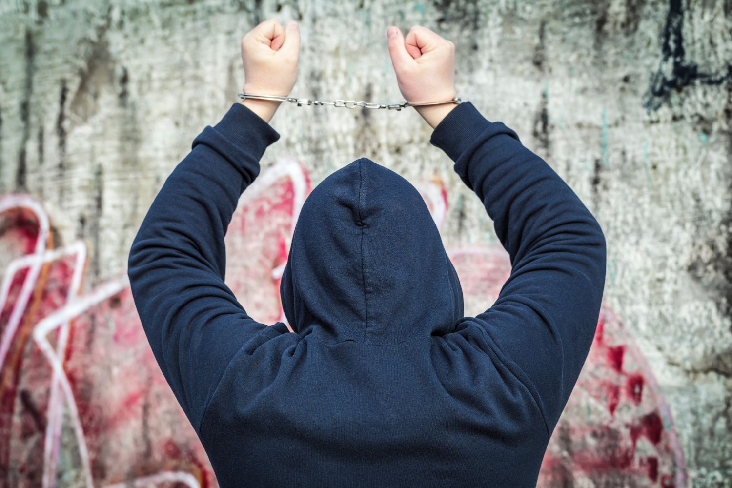 a man in a hoodie with his arms raised and handcuffed