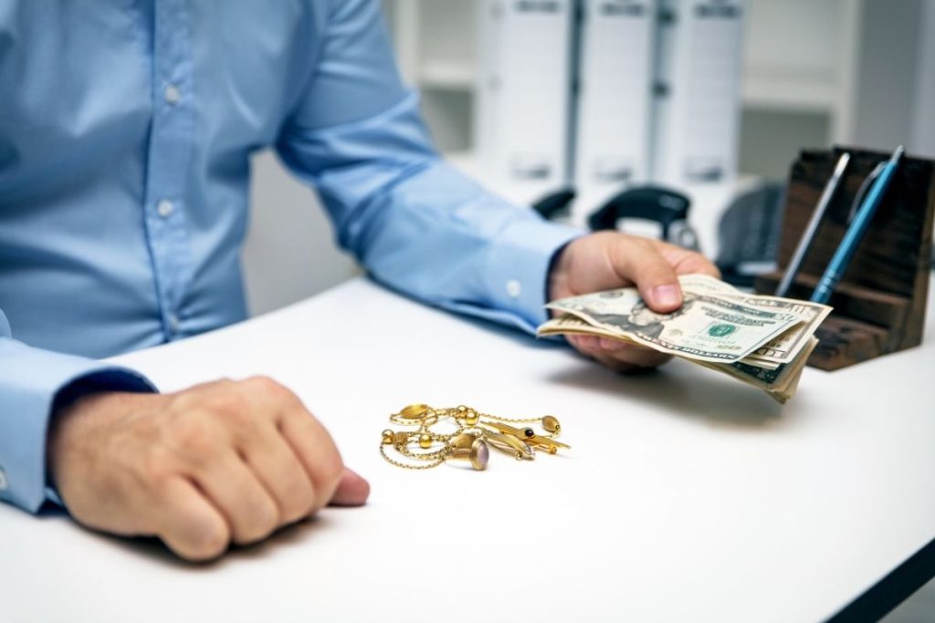 a man holding cash across a counter where some gold jewelry sits